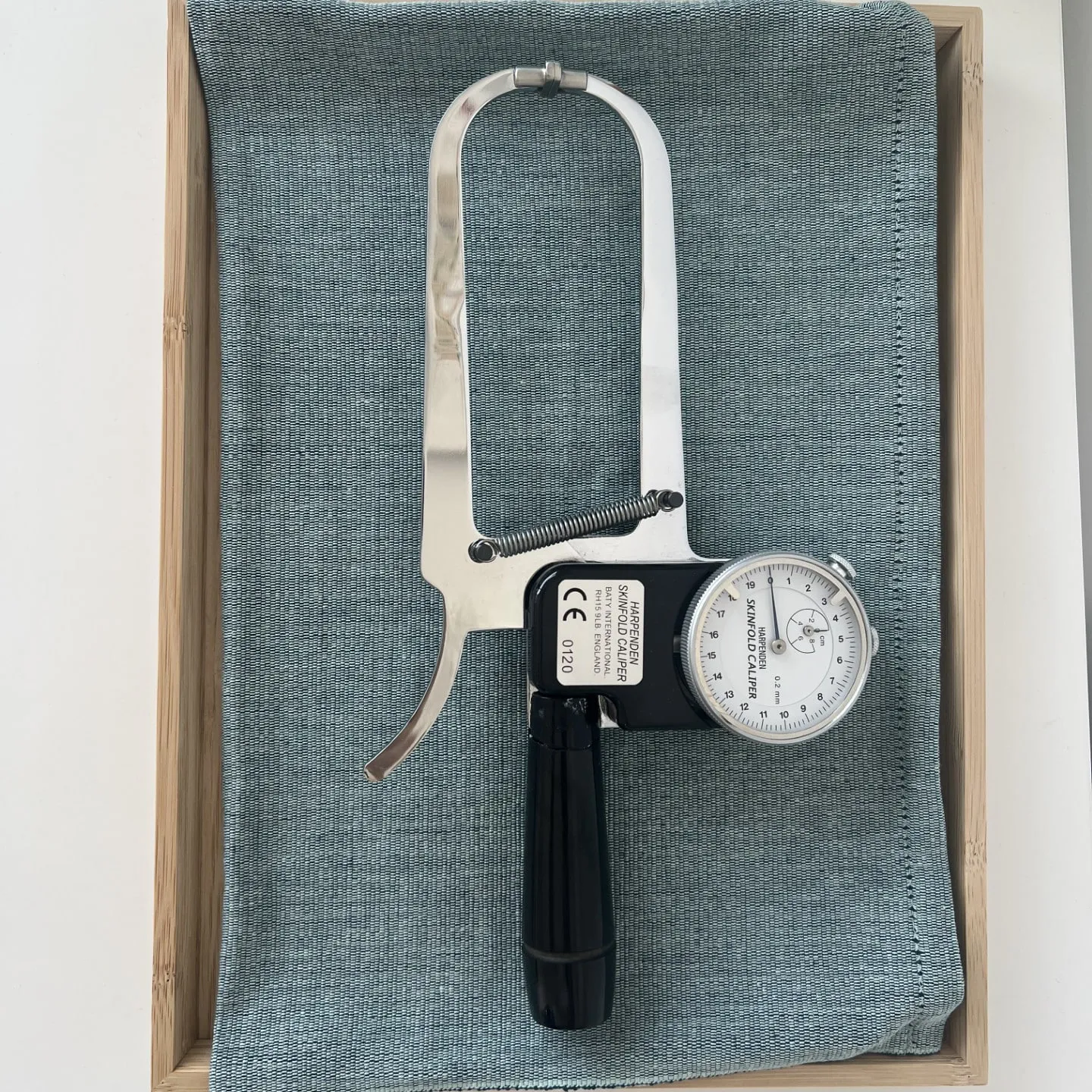 The caliper with its dial and measuring jaws, on a wooden tray